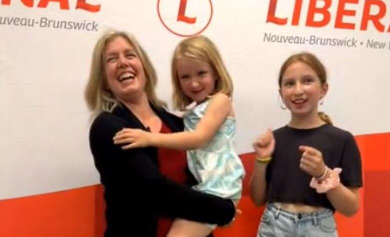 A woman, left, holding a little girl on her hip, with another girl standing next her.