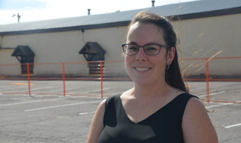 A woman stands in front of an arena, surrounded by construction fencing 