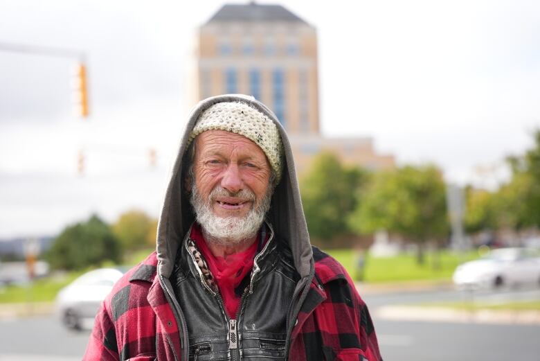 A man with a beard wearing a plaid flannel jacket. He's standing in view of Confederation Building.