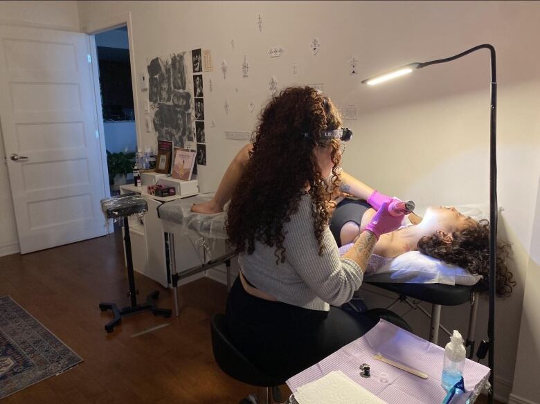 A woman lies on a bench as another woman tattoos her.