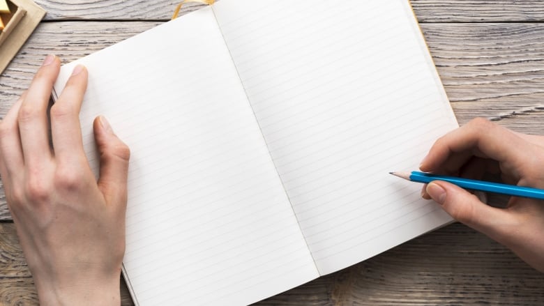 Two hands on an open notebook with blank pages. The right hand holds a blue pencil as if ready to write.