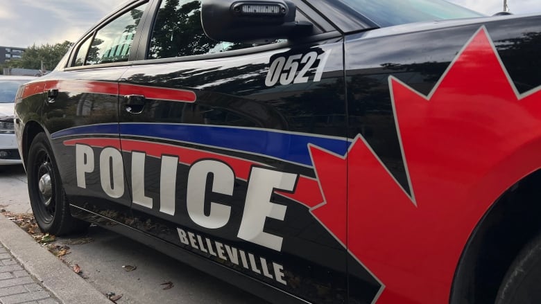 A close-up photo of the side of a black police car with a large maple leaf painted around the front wheel and the words 