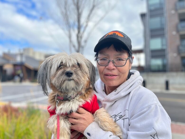 A woman standing, holding a small dog in a red t-shirt