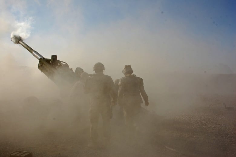 A gun crew fires artillery while obscured by a cloud of dust.