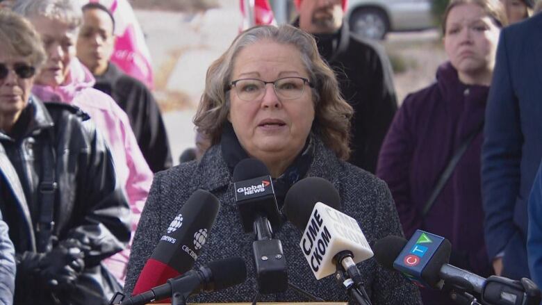 An old woman with grey hair can be seen standing at a podium, she is wearing a winter hat. 