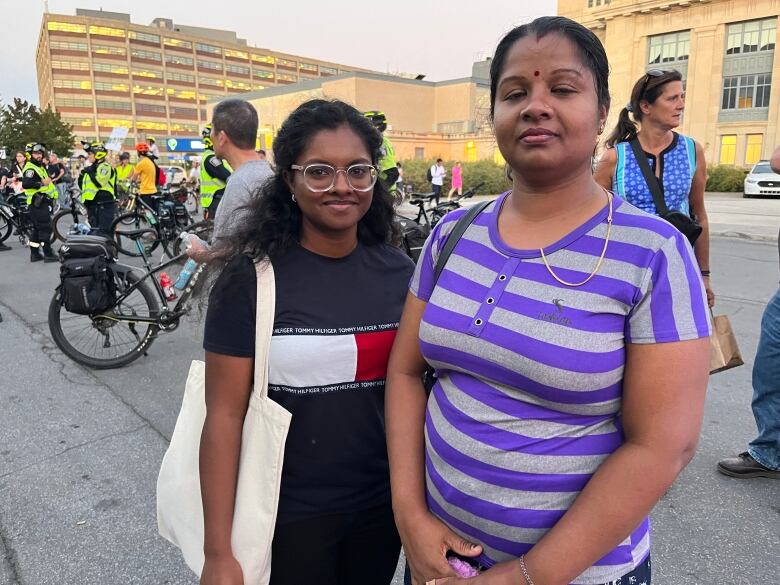 Two women smile at the camera with protestors behind them.