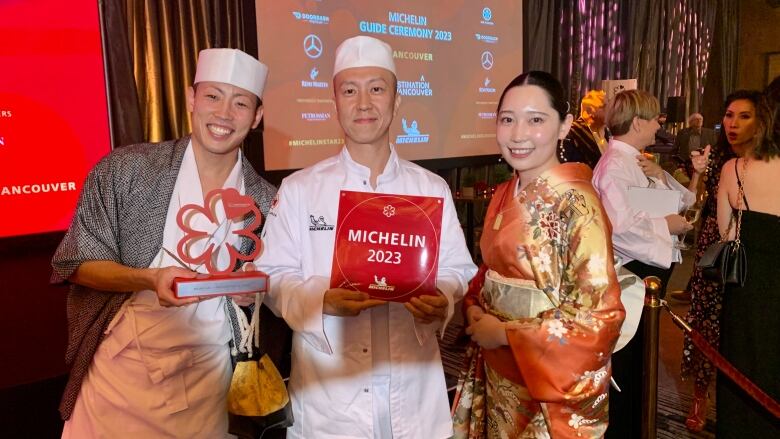 Three people stand holding a Michelin award. 