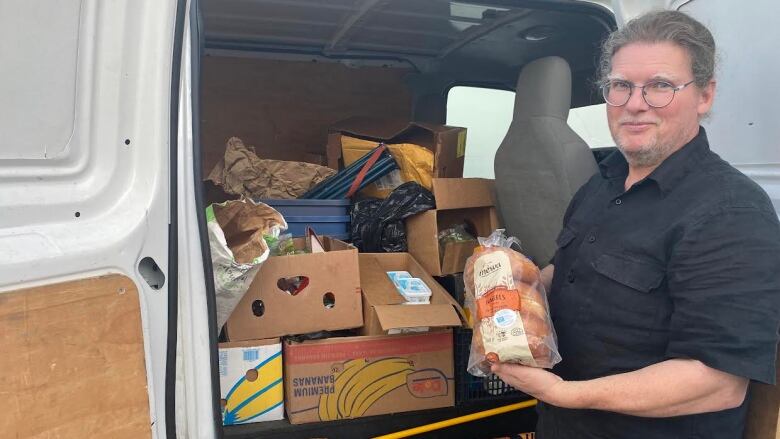 A man poses with food in front of a van.