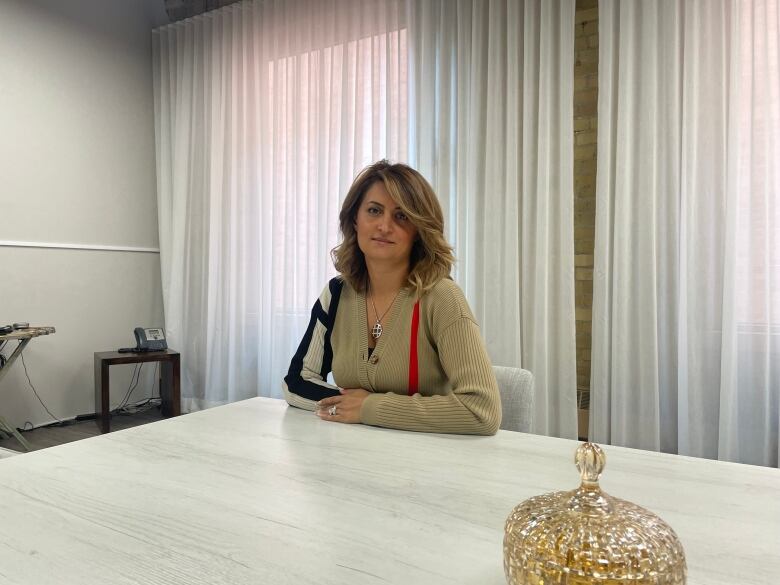 A middle-aged woman sits at a white board room table looking at the camera.