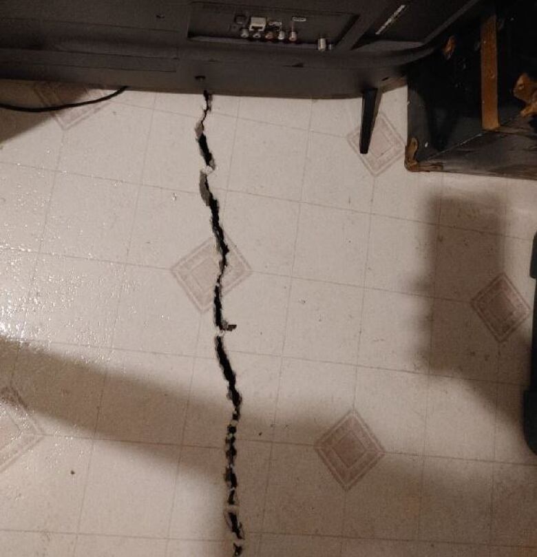 A crack in a floor, coming out from behind a piece of electronic equipment, is shown.