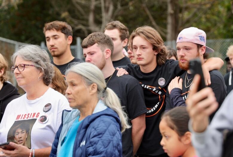 A group of Devon's friends are huddled together while people speak at the rally. 