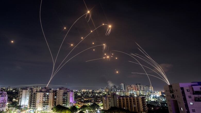 Streaks of orange light crisscross in the night sky above a city. 