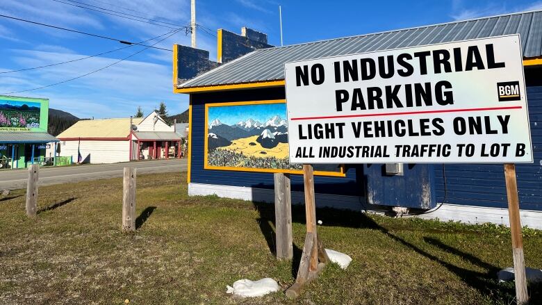 In a small town, historic buildings are seen with mountain murals painted on them, in front of which a sign says 