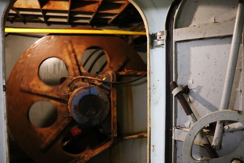 A big rusty wheel turns around a yellow cable below decks on a ferry. 