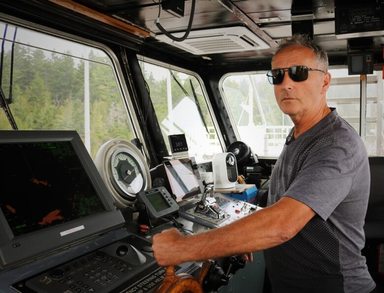 A man in a grey shirt and sunglasses stands on the bridge of the Peninsula Princess ferry. 