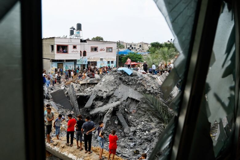 People gather around grey concrete rubble in Gaza.