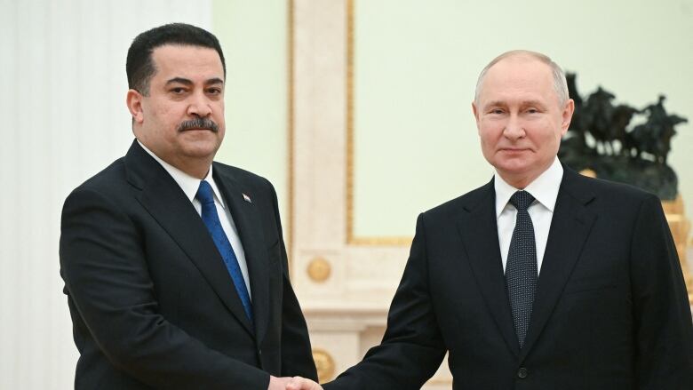 Two men in suits and ties, one with a dark mustache and the other balding, shake hands.