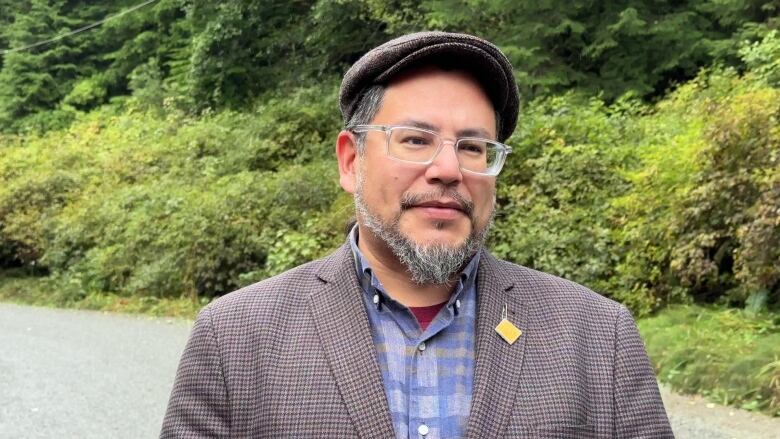 A man wearing a tweed jacket, a flat cap and glasses posing for the camera