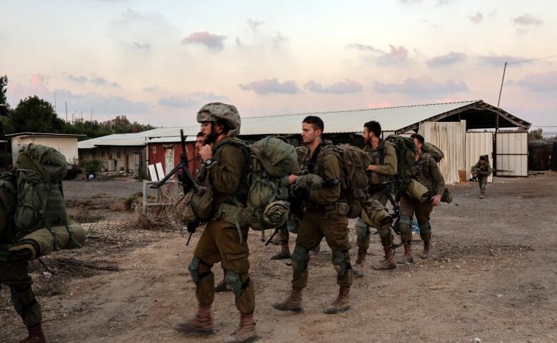 Israeli soldiers in dark green uniforms gather in a dusty street at dusk or dawn.