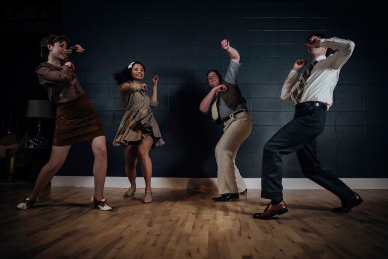 Four dancers, two women and two men, doing a swing dance with their arms in the air.