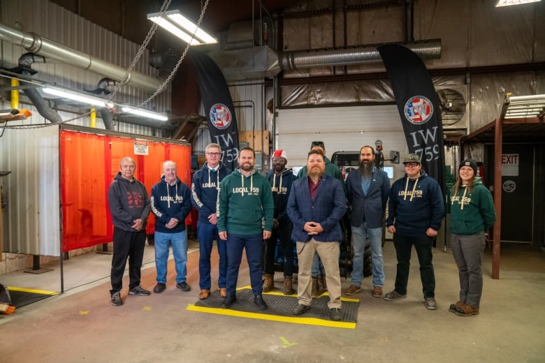 A group of people stand inside a welding shop setting.