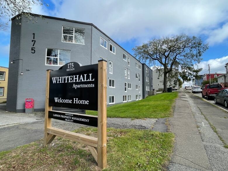 A grey apartment building with a sign in front of it that says 