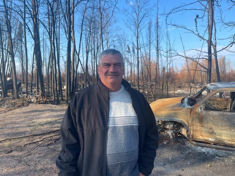 Man in front of burnt car, forest.