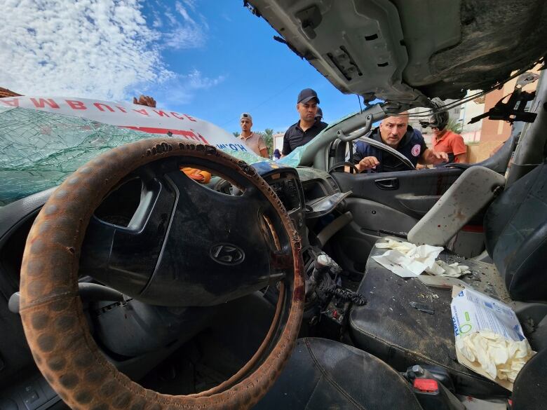 View from inside a damaged ambulance as people peer into it from the passenger window. 