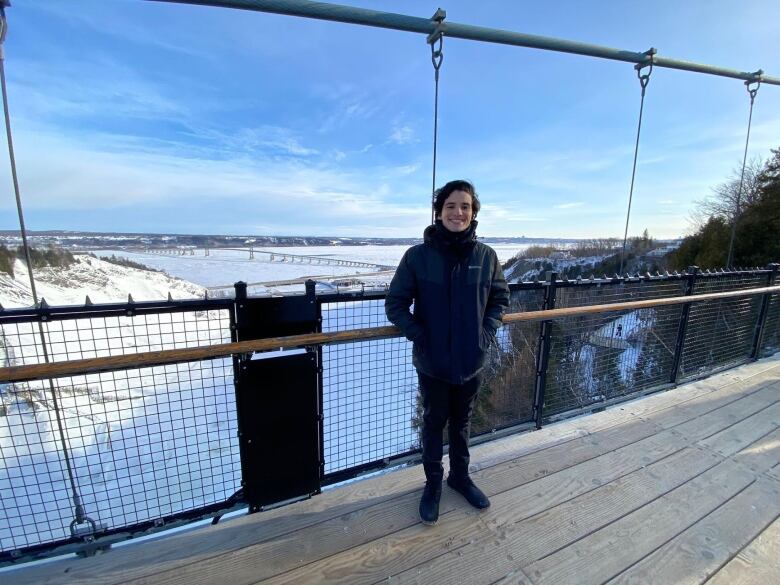 A man in a warm coat stands on a bridge overlooking a lake in winter.