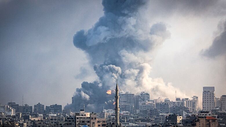 A huge grey smoke cloud looms over a crowded skyline with a minaret in its centre.