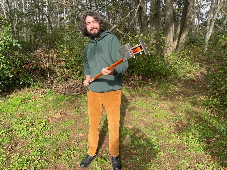 A man holds a large tool used to dig out shrubs 