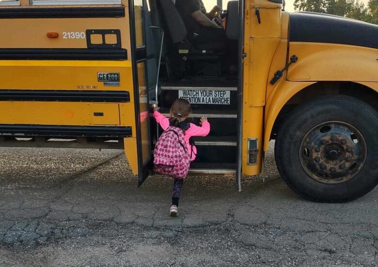 A little girl dressed in pink getting onto a school bus