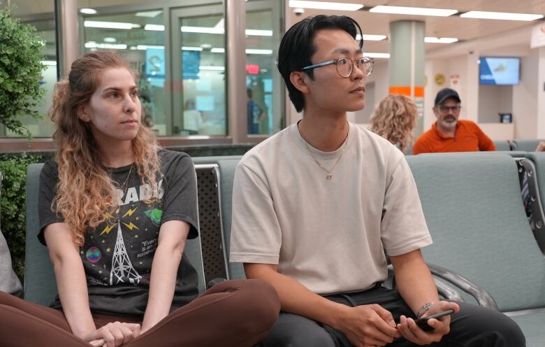 A man and woman wait on seats in an airport. 