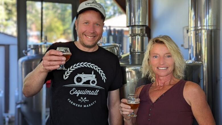 Man and a woman inside a brewery posing with beer in their hands.