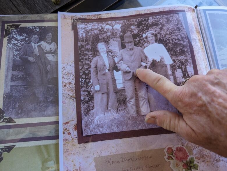 A hand pointing at an old photograph showing a man with a hat in the middle and two women either side of him. 