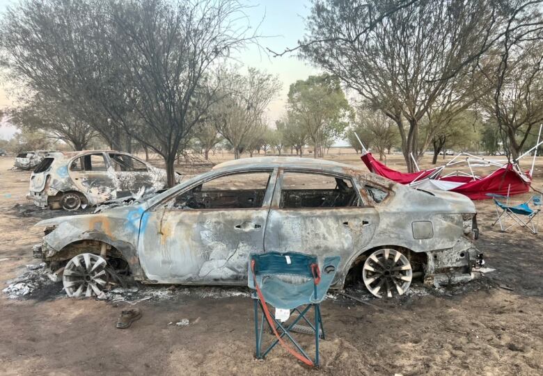 A burned out car with a camping chair in front.