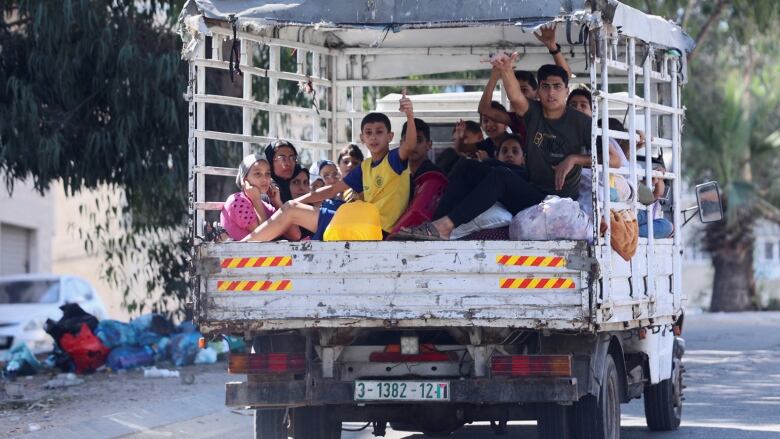 A truck carrying people in the back, with some waving or giving a thumbs up.