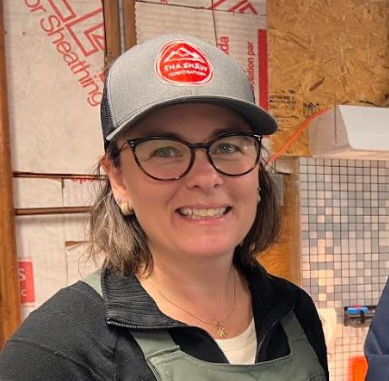 A woman wearing glasses and a ball cap.