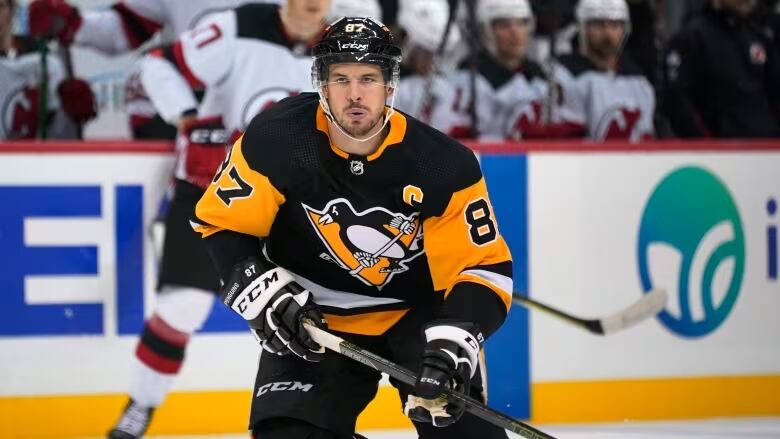 A hockey player in a black and yellow Pittsburgh Penguins uniform skates while holding a hockey stick.