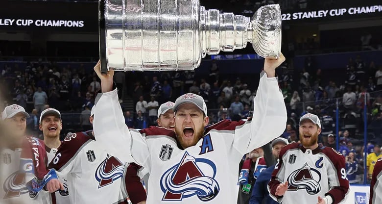 A hockey player in a white Colorado Avalanches uniform hoists the Stanley Cup.