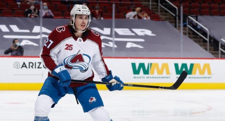 A hockey player in a white, red and blue jersey skating on the ice.