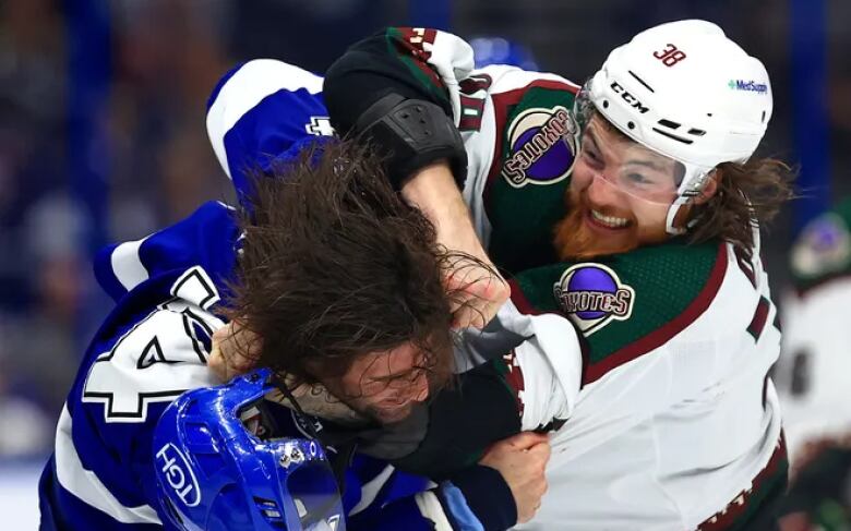 A hockey player in a white uniform punches a hockey player in a blue uniform.