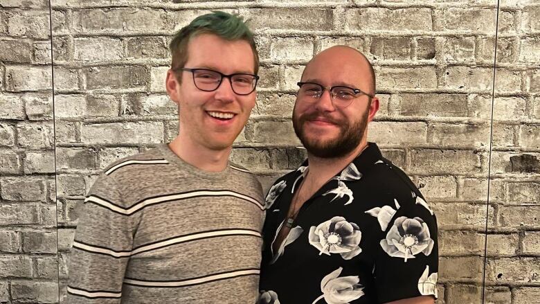 Two men standing in front of a brick wall.