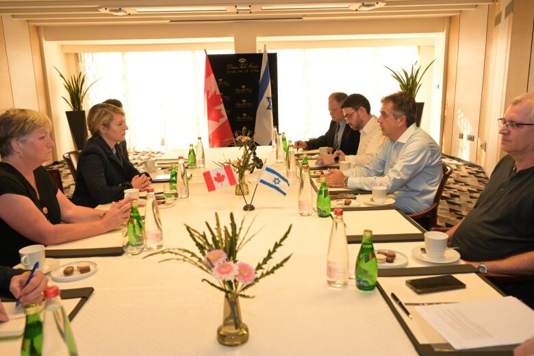 Government officials sit at a table with a centrepiece that holds a Canadian and Israeli flag.