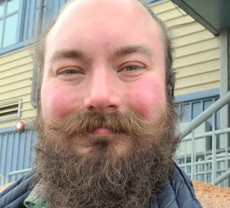 A balding man with a long brown beard poses for a photo. 