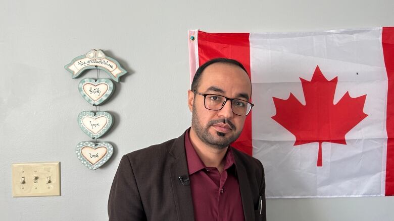 A bald man in a suit standing against Canadian flag.