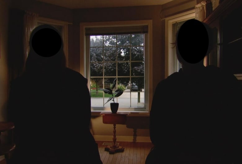 Two people sit in chairs with their backs to the camera. They are in shadow and their faces are not visible. They are looking out a living room window to the street outside.