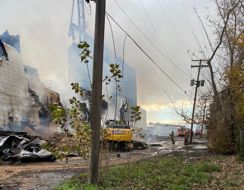 Smoke surrounds a building. An excavator sits in front of it.