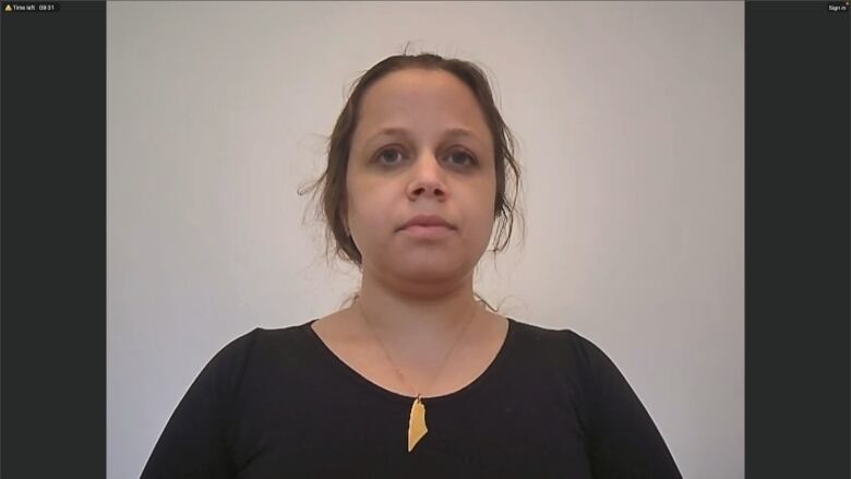 A woman with her hair pulled back and wearing a black top speaks to the camera.