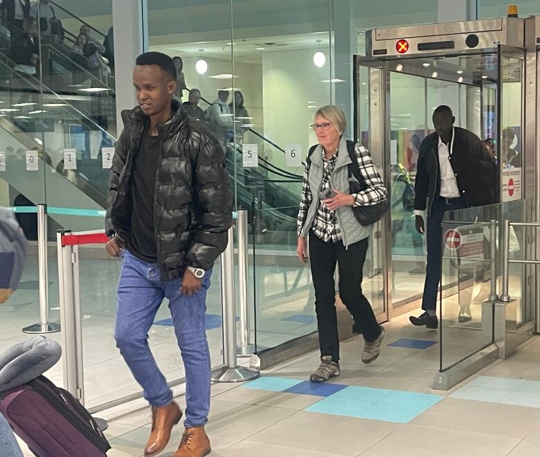 A man wearing jeans and a black coat arriving at an airport.